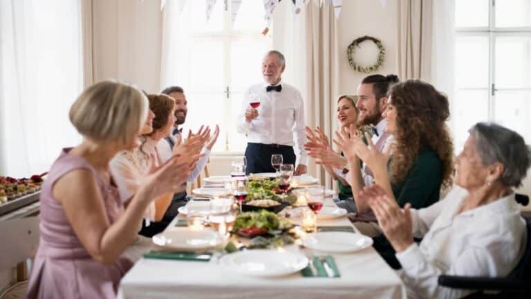 Guests clapping and smiling at a wedding reception dinner table.