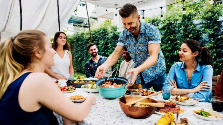 Freshly prepared gourmet dishes served at outdoor event with smiling guests and chef.