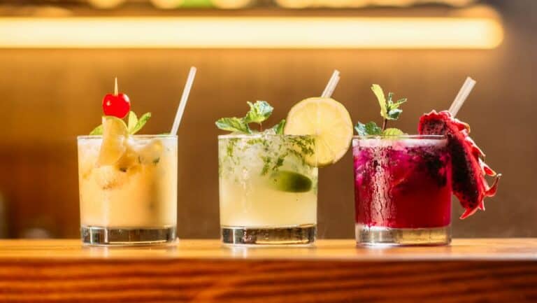 Three colorful non-alcoholic drinks with garnishes on a wooden bar.