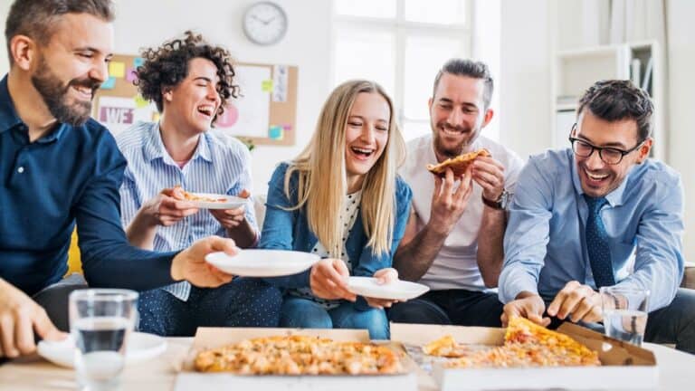 A lively group of friends enjoying pizza together in a bright, modern kitchen.