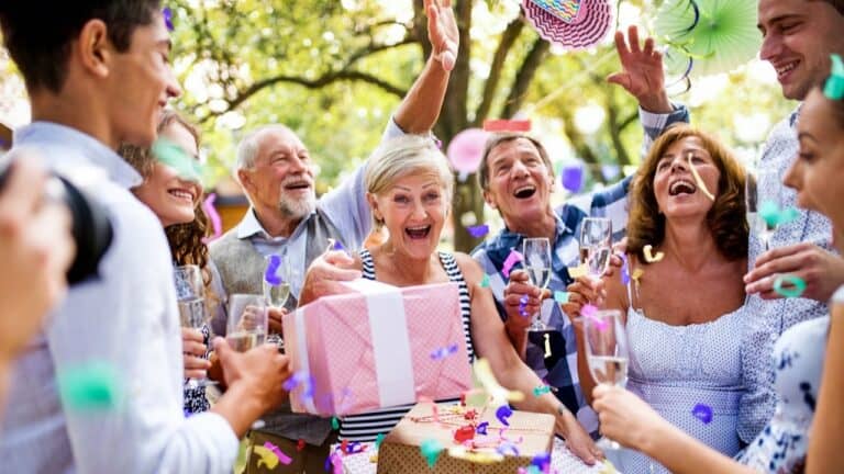 Group of seniors celebrating at a retirement party outdoors with gifts and drinks.