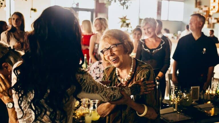 Joyful elderly woman at retirement party laughing with guests.