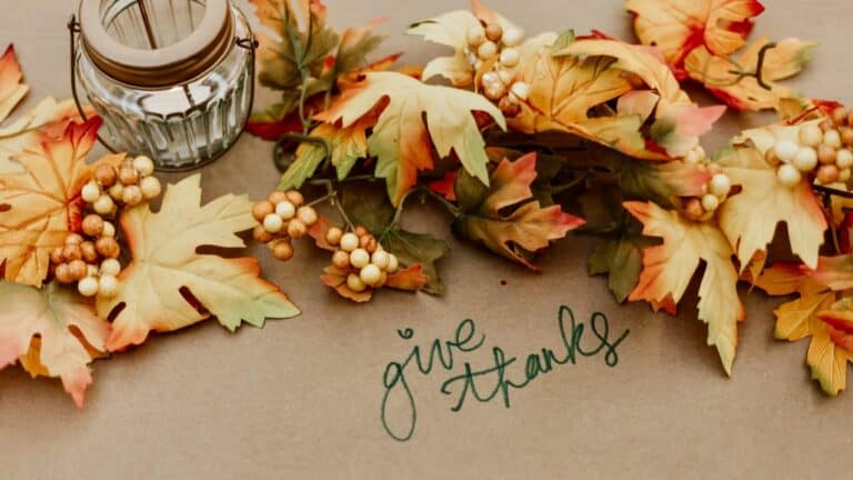 Autumn-themed table with a candle, leaves, berries, and a 'give thanks' note.