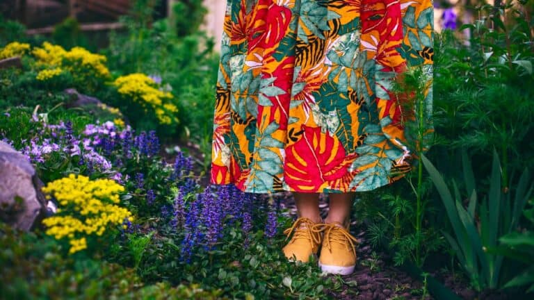 Person standing in a lush garden with colorful flowers and vibrant dress.