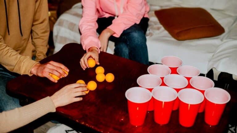 People playing beer pong with orange balls and red cups at a party.