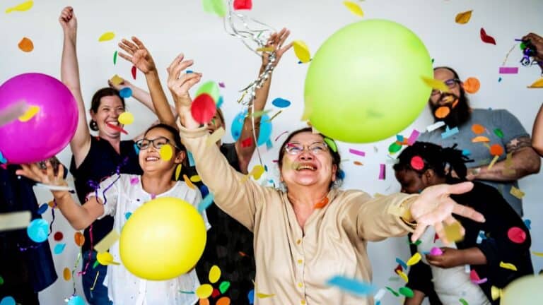 Group of adults celebrating with balloons and confetti at a party.