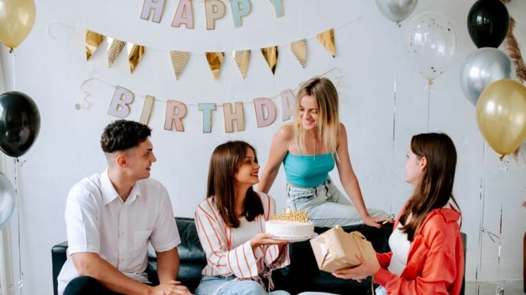 Group celebrating birthday with cake, gifts, and festive decorations.