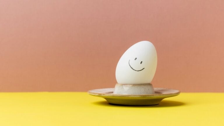 Smiling egg on a small plate with a pink and yellow background.