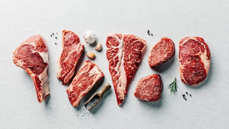 Assorted raw steak cuts with seasoning and herbs for cooking.