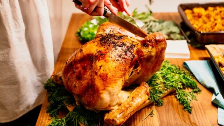 Juicy roasted turkey on a wooden cutting board with herbs and spices.