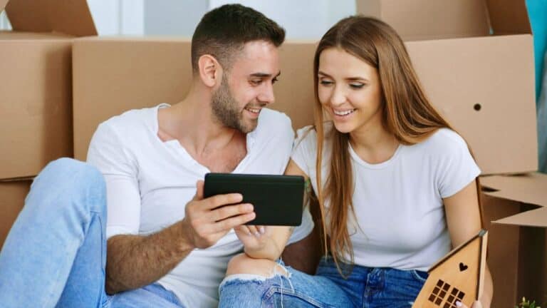 Happy couple looking at a smartphone during housewarming preparations.