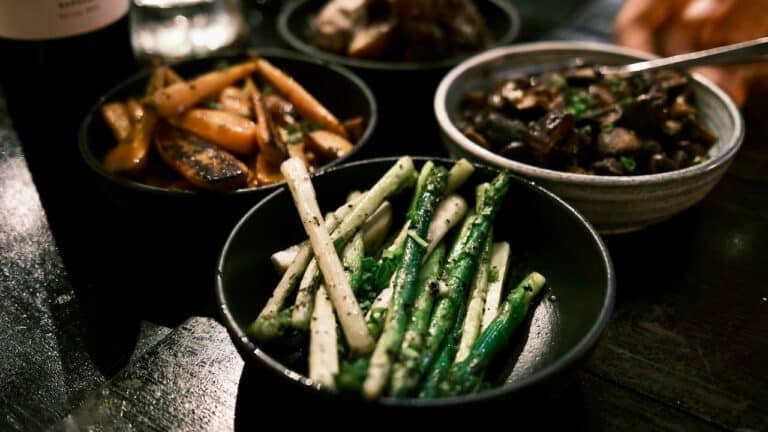 Vegetarian Asian dishes with green beans, eggplant, and bamboo shoots on a dark table.