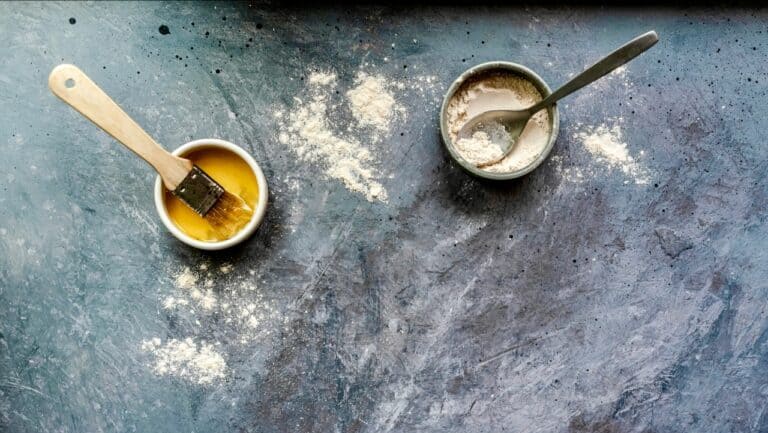 Baking ingredients including flour, baking powder substitute, and a brush on a dark surface.