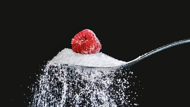 Close-up of a spoonful of baking soda with a raspberry on top against a black background.