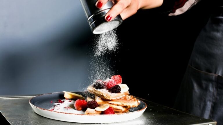 Person sprinkling powdered sugar on a stack of pancakes with berries.