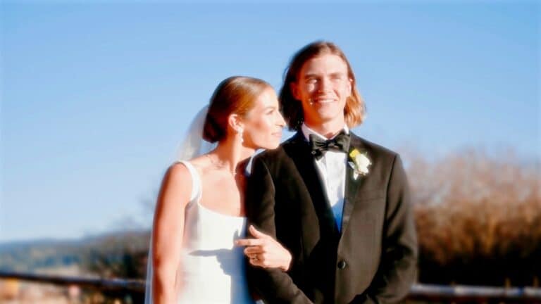 Bride and groom smiling outdoors on wedding day with clear blue sky.