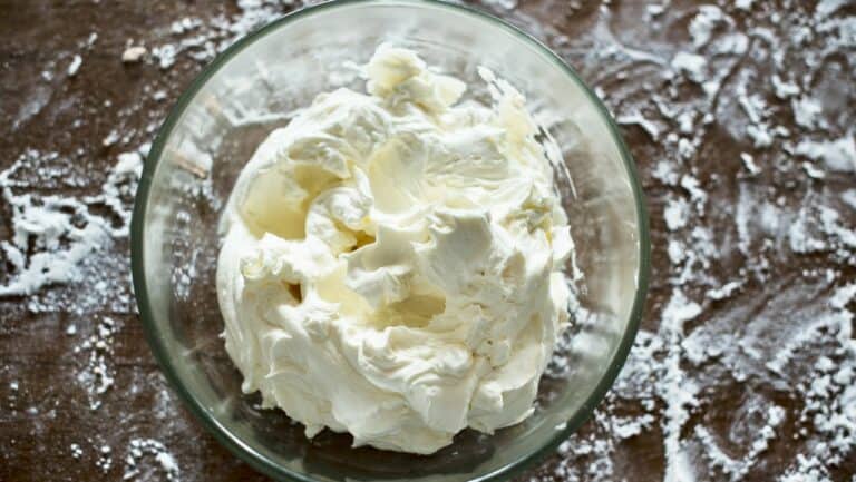 Cream cheese in a glass bowl on a floured surface for baking or cooking.