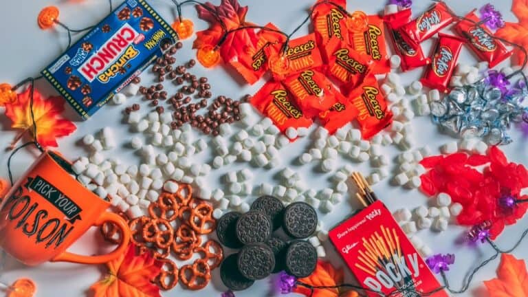 Halloween party snacks and candies arranged on a table with autumn leaves.