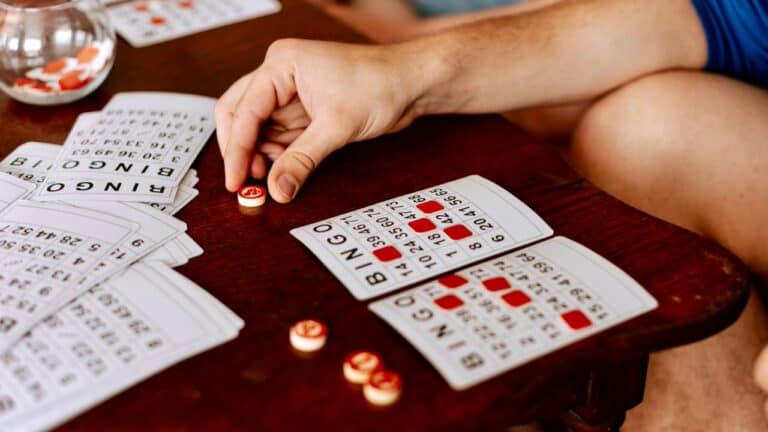 Person playing bingo with cards and chips on a wooden table.