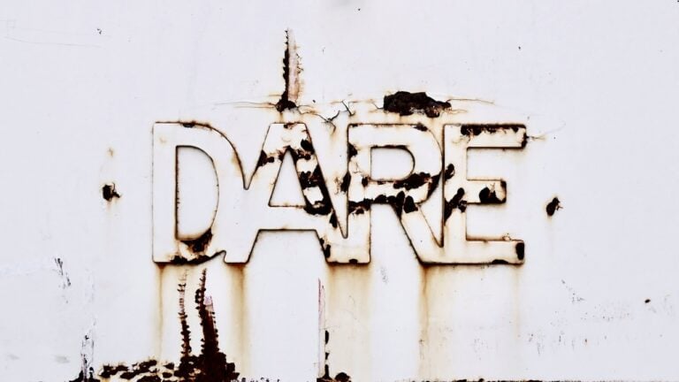 Rusty metal sign spelling 'DARE' on a weathered wall.