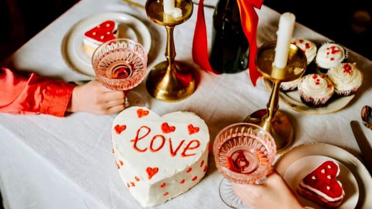 Heart-shaped Valentine's cake with 'love' inscription and cupcakes on a decorated table.