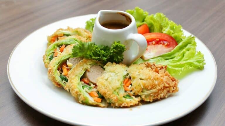 Vegetarian spring rolls with dipping sauce and fresh vegetables on a white plate.