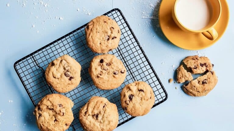 Chocolate chip cookies cooling on a wire rack with a glass of milk.